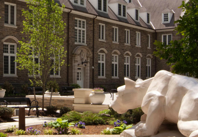 A photograph of a statue of the Penn State Nittany Lion mascot looking toward a building on campus.